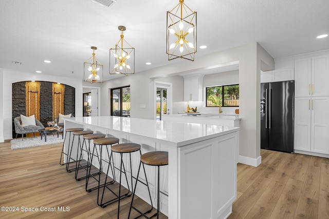 kitchen with white cabinets, decorative light fixtures, light wood-type flooring, and stainless steel refrigerator with ice dispenser