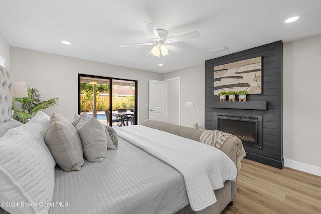 bedroom with ceiling fan, a large fireplace, light hardwood / wood-style floors, a textured ceiling, and access to outside