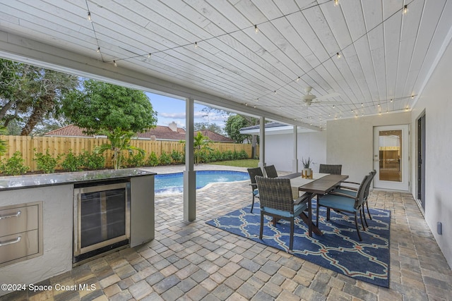 view of patio featuring ceiling fan, a fenced in pool, an outdoor bar, and wine cooler