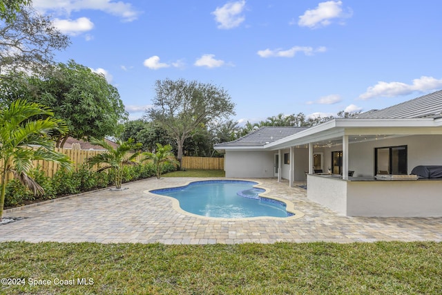 view of pool featuring an outdoor kitchen, a patio, area for grilling, exterior bar, and a yard