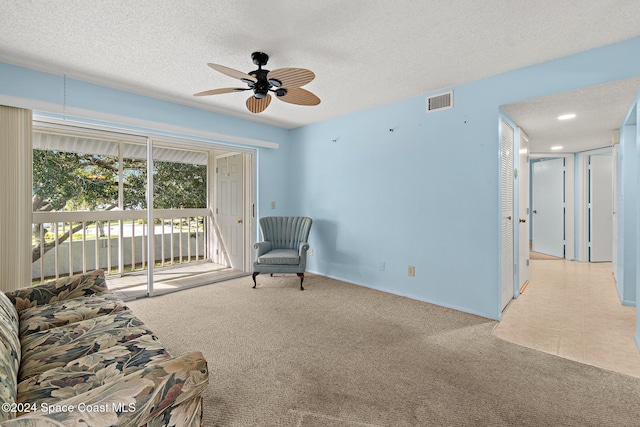 living area with ceiling fan, light colored carpet, and a textured ceiling