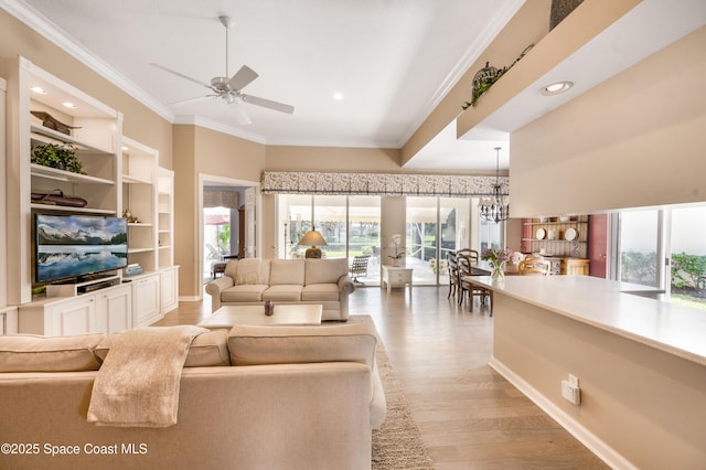 living room with a wealth of natural light, built in features, ceiling fan with notable chandelier, and light wood-type flooring