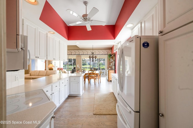 kitchen featuring pendant lighting, ceiling fan with notable chandelier, white refrigerator, white cabinetry, and kitchen peninsula