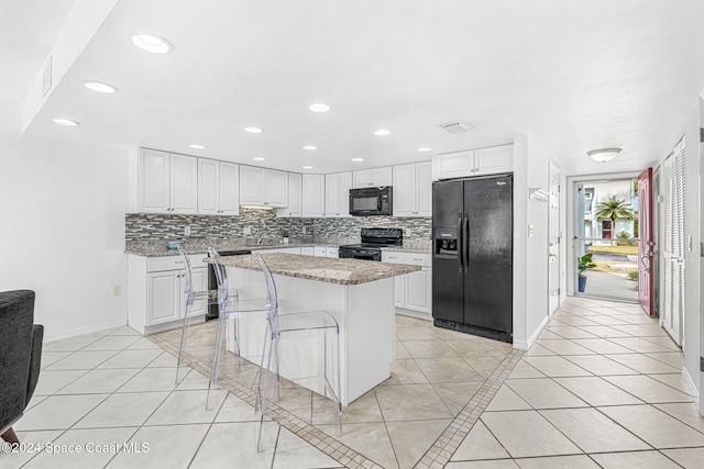 kitchen with white cabinetry, a center island, a kitchen bar, light tile patterned floors, and black appliances