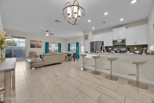 kitchen with backsplash, white cabinets, ceiling fan with notable chandelier, a kitchen bar, and stainless steel appliances