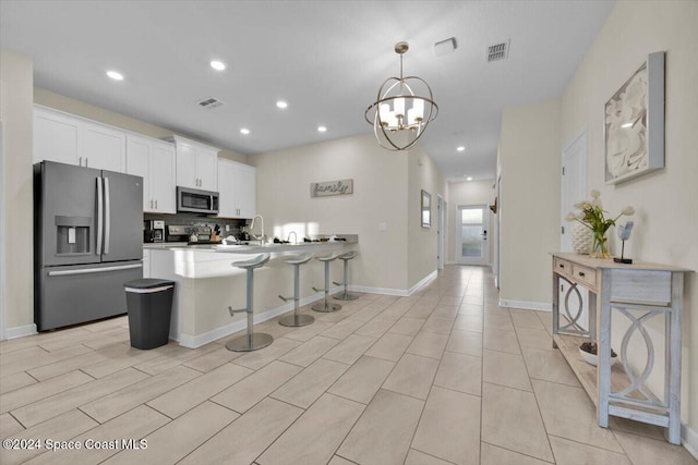 kitchen featuring a kitchen bar, appliances with stainless steel finishes, kitchen peninsula, decorative light fixtures, and white cabinets