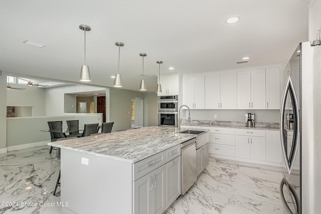 kitchen with stainless steel appliances, ceiling fan, a center island with sink, white cabinetry, and hanging light fixtures