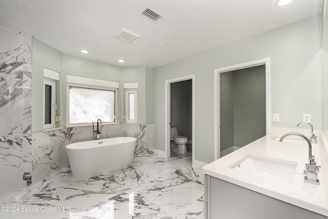 bathroom with a bathing tub, vanity, a textured ceiling, and toilet