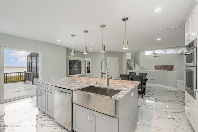 kitchen featuring stainless steel appliances, a kitchen island with sink, sink, decorative light fixtures, and white cabinetry