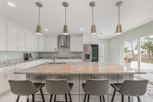 kitchen featuring pendant lighting, wall chimney exhaust hood, a spacious island, and stainless steel refrigerator with ice dispenser