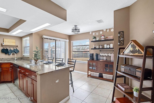 kitchen with dishwasher, a kitchen breakfast bar, sink, light tile patterned floors, and light stone counters