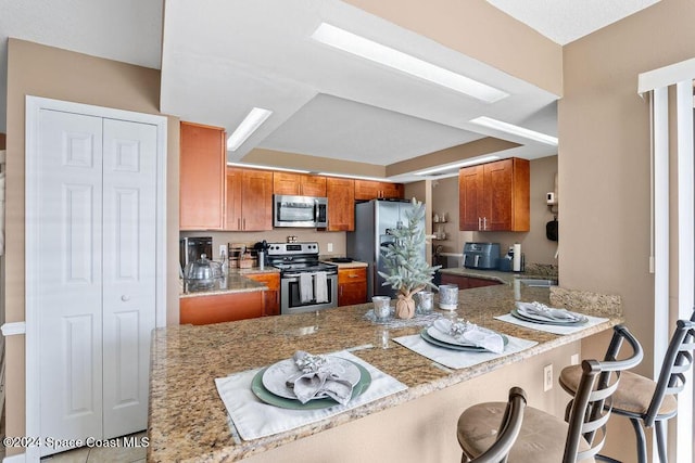 kitchen featuring kitchen peninsula, appliances with stainless steel finishes, a kitchen bar, and light stone counters