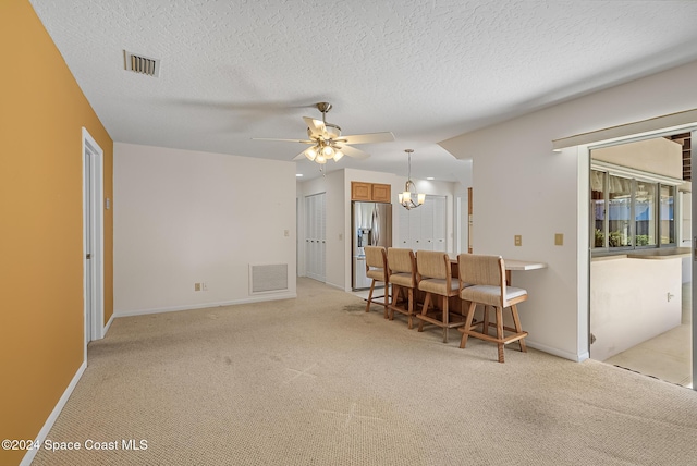 carpeted living room featuring ceiling fan with notable chandelier and a textured ceiling