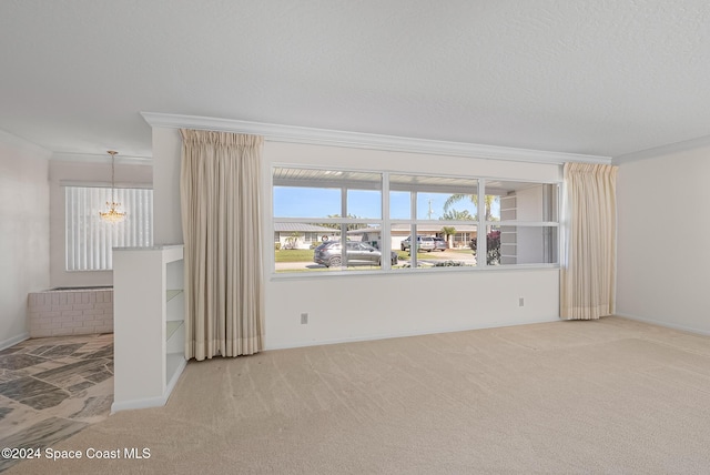 carpeted empty room with ornamental molding, a textured ceiling, and an inviting chandelier