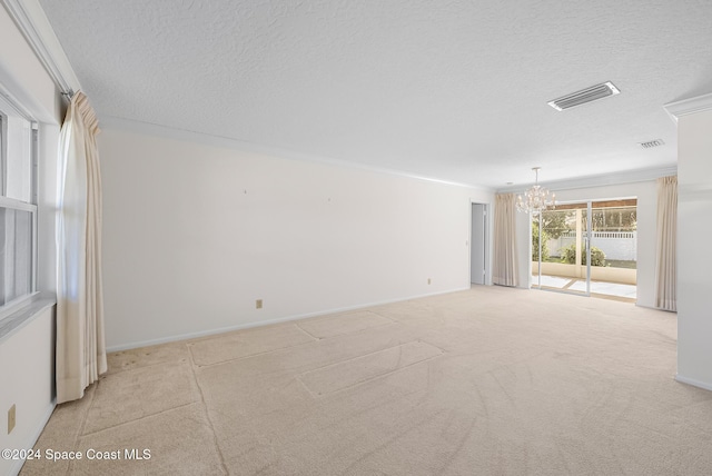 carpeted empty room featuring ornamental molding, a textured ceiling, and an inviting chandelier