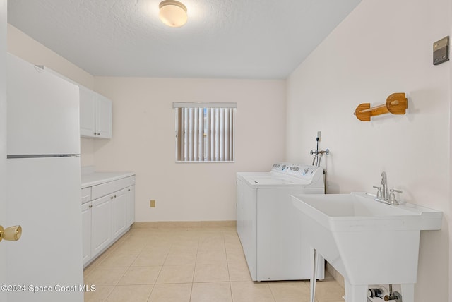 laundry room with washing machine and clothes dryer, sink, cabinets, a textured ceiling, and light tile patterned floors