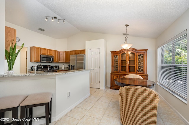 kitchen with light stone countertops, kitchen peninsula, stainless steel appliances, light tile patterned floors, and decorative light fixtures