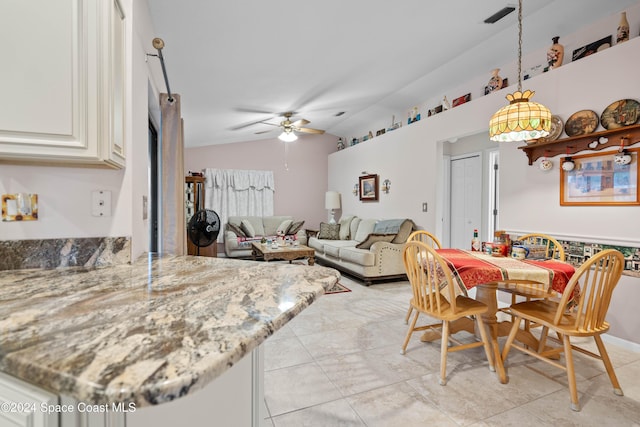 kitchen with light stone counters, vaulted ceiling, ceiling fan, white cabinets, and hanging light fixtures