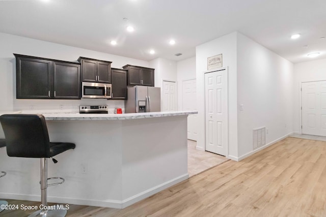 kitchen featuring a kitchen breakfast bar, stainless steel appliances, light hardwood / wood-style flooring, and light stone counters