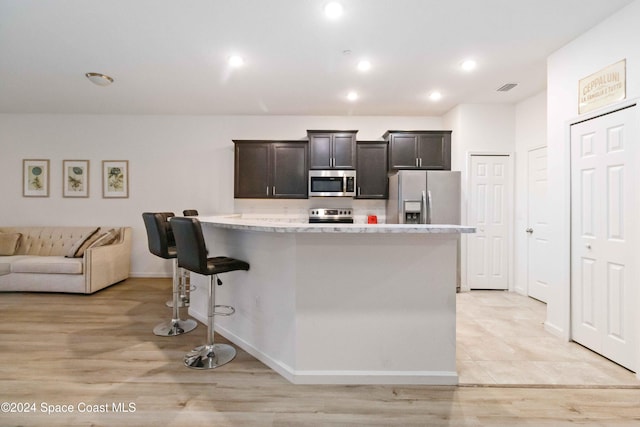 kitchen with dark brown cabinetry, light stone countertops, a center island, stainless steel appliances, and a kitchen bar