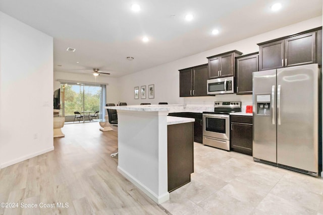 kitchen featuring a breakfast bar, ceiling fan, light wood-type flooring, appliances with stainless steel finishes, and dark brown cabinetry