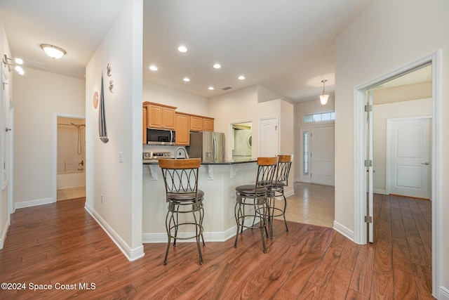 kitchen featuring sink, stainless steel appliances, kitchen peninsula, a kitchen bar, and hardwood / wood-style flooring