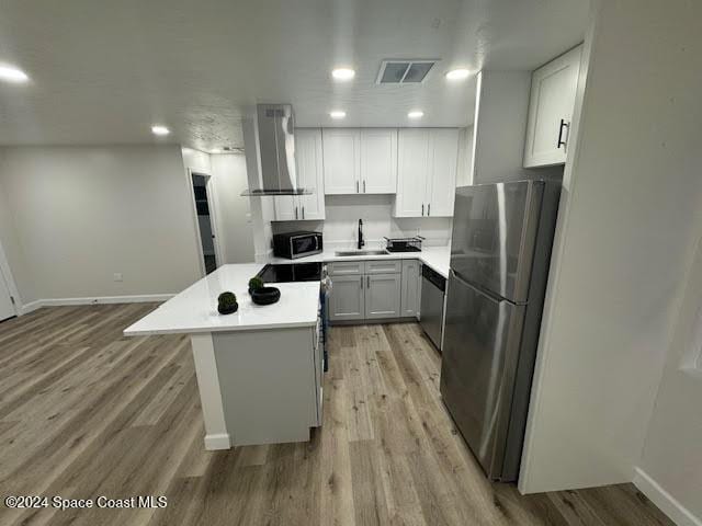 kitchen featuring white cabinets, wall chimney range hood, sink, and appliances with stainless steel finishes