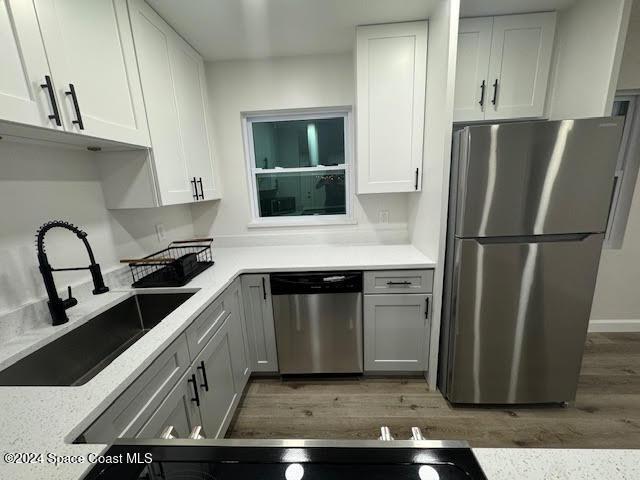 kitchen featuring wood-type flooring, appliances with stainless steel finishes, white cabinets, and sink