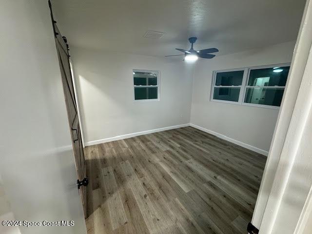 spare room featuring a barn door, hardwood / wood-style flooring, and ceiling fan