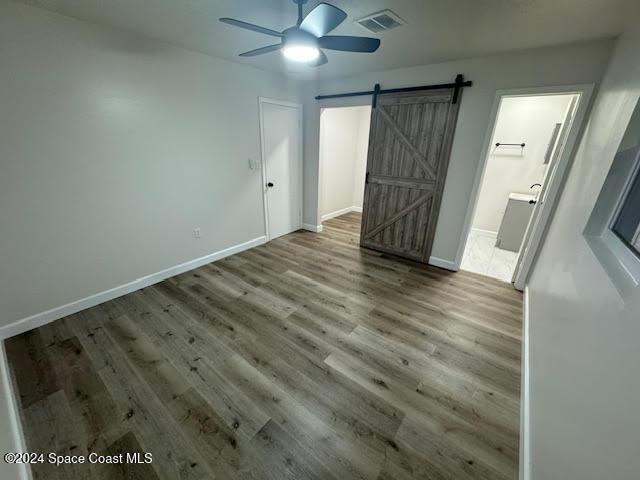 unfurnished bedroom with hardwood / wood-style floors, ensuite bathroom, a barn door, and ceiling fan