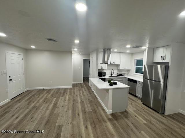 kitchen with stainless steel refrigerator, sink, wall chimney exhaust hood, hardwood / wood-style floors, and white cabinets