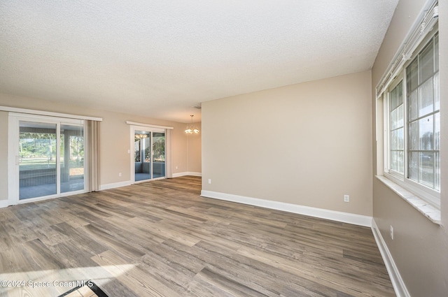 unfurnished room with a chandelier, a textured ceiling, and hardwood / wood-style flooring