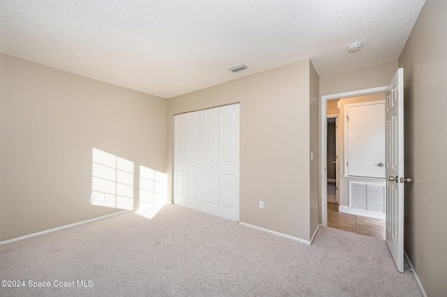 unfurnished bedroom with a closet, light colored carpet, and a textured ceiling