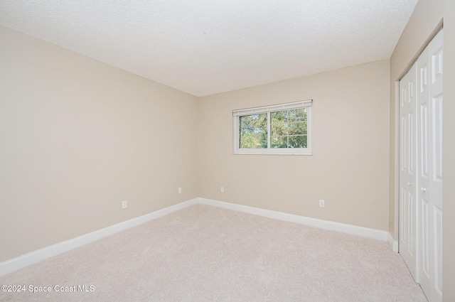 unfurnished bedroom featuring a textured ceiling, light carpet, and a closet