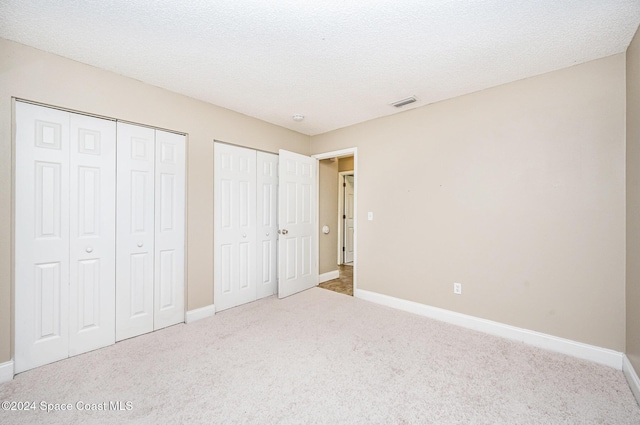 unfurnished bedroom with carpet, a textured ceiling, and multiple closets