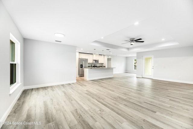 unfurnished living room with light hardwood / wood-style flooring, a raised ceiling, and ceiling fan