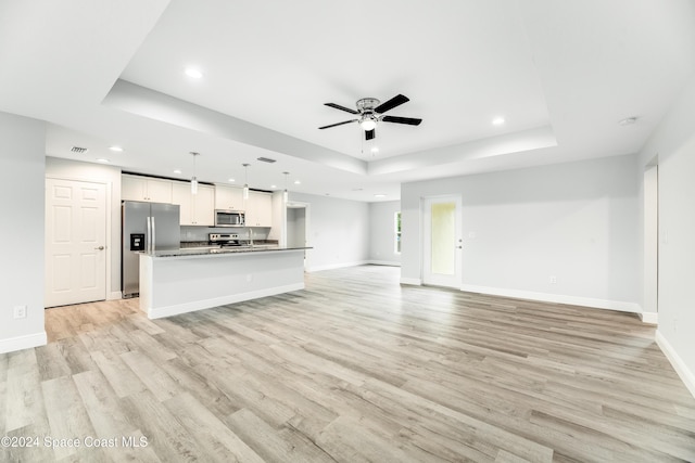 unfurnished living room featuring ceiling fan, light hardwood / wood-style flooring, and a tray ceiling