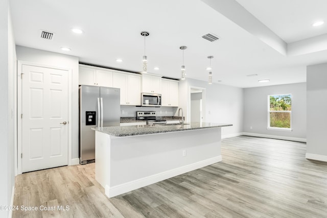 kitchen featuring white cabinets, appliances with stainless steel finishes, a kitchen island with sink, and dark stone counters