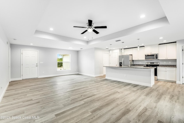 unfurnished living room with light wood-type flooring, a tray ceiling, ceiling fan, and sink