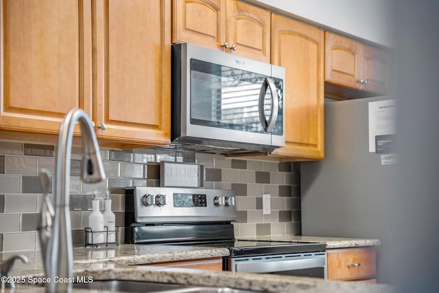 kitchen with tasteful backsplash, light stone countertops, and appliances with stainless steel finishes