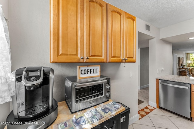 kitchen with light stone countertops, dishwasher, light tile patterned floors, and a textured ceiling