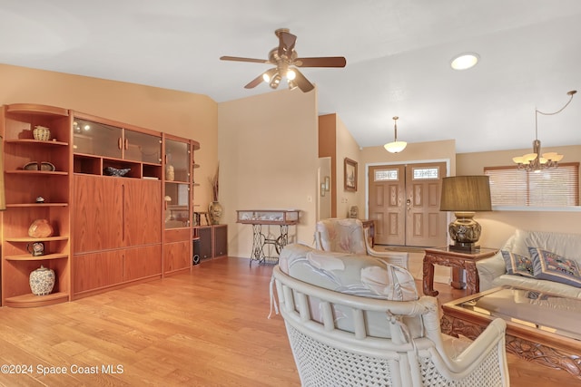 living room featuring light hardwood / wood-style flooring, ceiling fan with notable chandelier, and vaulted ceiling