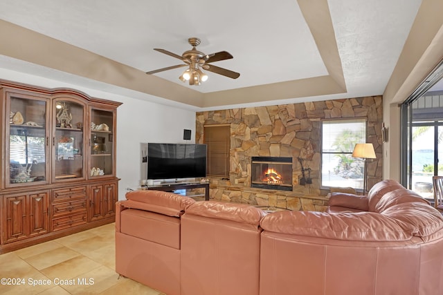 living room with a fireplace, light tile patterned floors, a raised ceiling, and ceiling fan