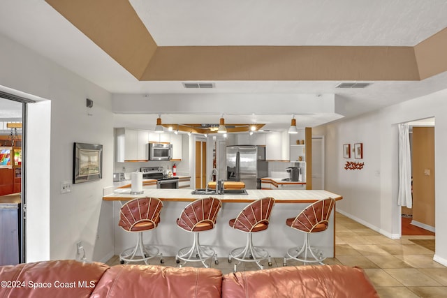 kitchen with sink, kitchen peninsula, appliances with stainless steel finishes, white cabinetry, and a breakfast bar area