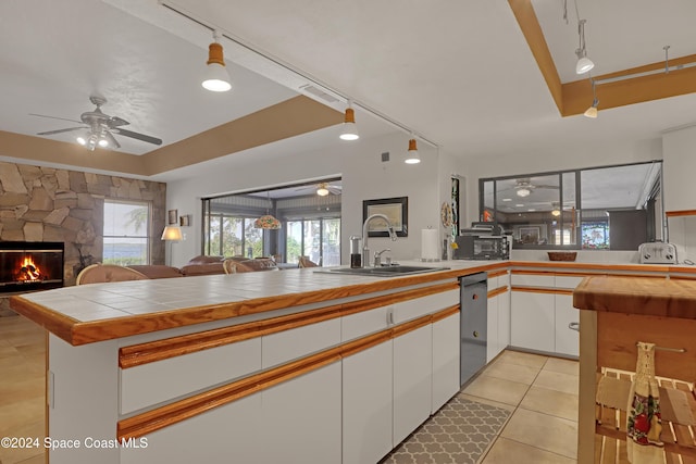 kitchen featuring sink, kitchen peninsula, tile countertops, decorative light fixtures, and white cabinets