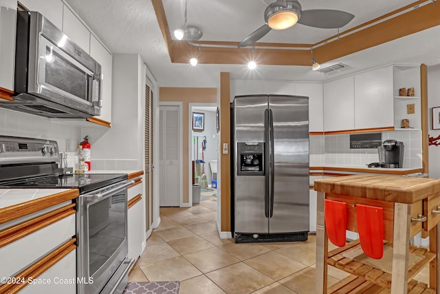 kitchen with backsplash, white cabinets, tile counters, light tile patterned flooring, and stainless steel appliances