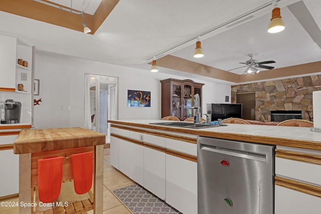 kitchen with ceiling fan, dishwasher, light tile patterned flooring, a fireplace, and white cabinets