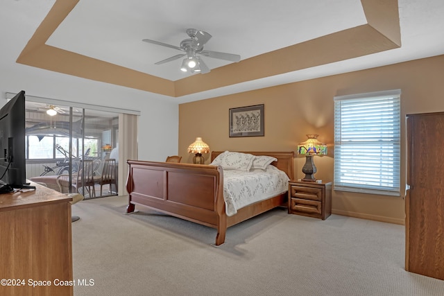 carpeted bedroom with a raised ceiling and ceiling fan