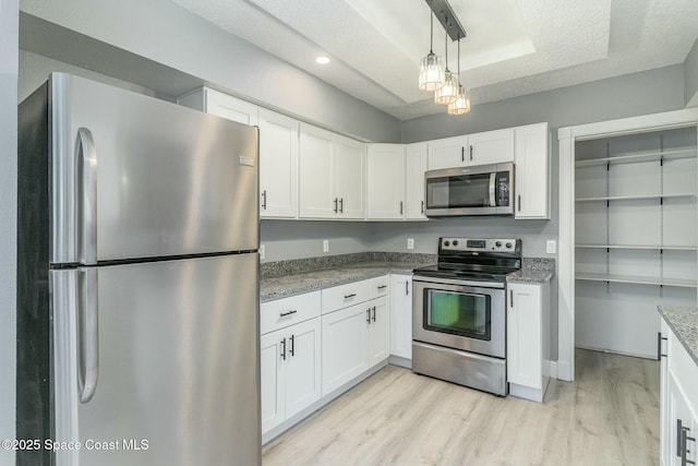 kitchen featuring light stone countertops, stainless steel appliances, a raised ceiling, light hardwood / wood-style flooring, and white cabinets