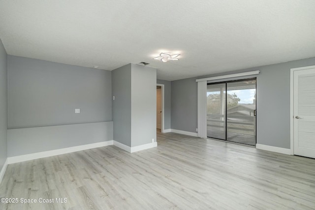 empty room with a textured ceiling and light hardwood / wood-style flooring